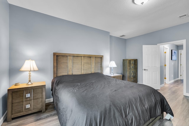 bedroom with baseboards, wood finished floors, vaulted ceiling, and a textured ceiling