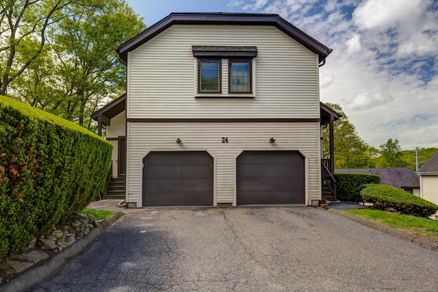 view of side of home with an attached garage, asphalt driveway, and stairway