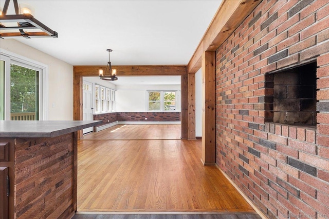 kitchen featuring a notable chandelier, wood finished floors, brick wall, and a healthy amount of sunlight