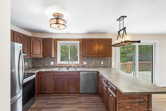 kitchen featuring a peninsula, dark wood-type flooring, tasteful backsplash, a sink, and appliances with stainless steel finishes