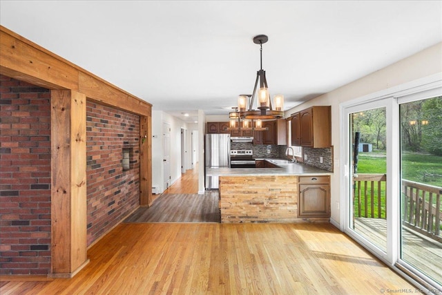 kitchen featuring under cabinet range hood, light wood-type flooring, a sink, a chandelier, and stainless steel appliances