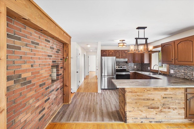 kitchen with stainless steel appliances, a sink, light wood-style flooring, and a peninsula