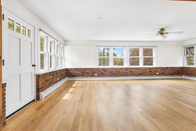empty room featuring baseboard heating, a ceiling fan, light wood-type flooring, and brick wall