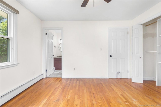 unfurnished bedroom featuring a baseboard radiator, ensuite bath, a ceiling fan, baseboards, and light wood-type flooring