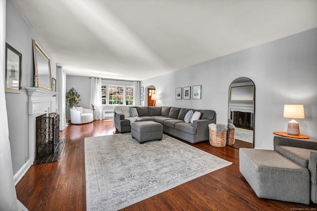 living room featuring a fireplace with raised hearth, arched walkways, and dark wood-style floors