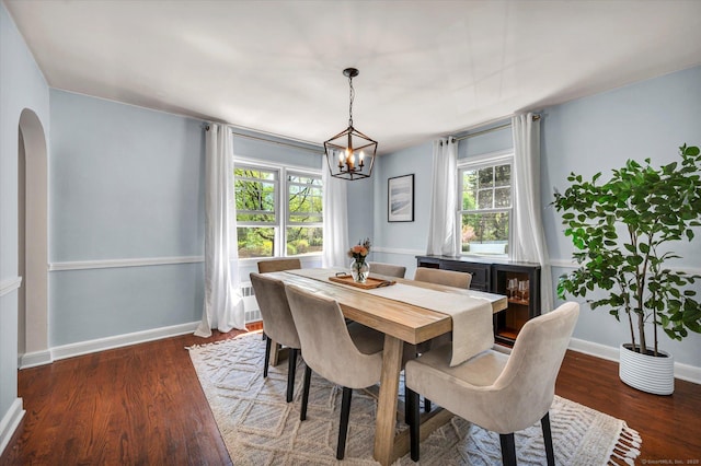 dining room featuring a chandelier, dark wood-style floors, arched walkways, and baseboards