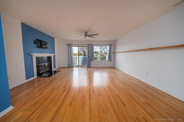 unfurnished living room featuring visible vents, a glass covered fireplace, light wood-style floors, baseboards, and a ceiling fan