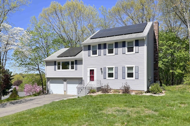 split level home with a chimney, solar panels, a front yard, and a garage