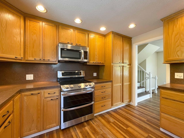 kitchen featuring dark wood-style flooring, stainless steel appliances, dark countertops, and tasteful backsplash
