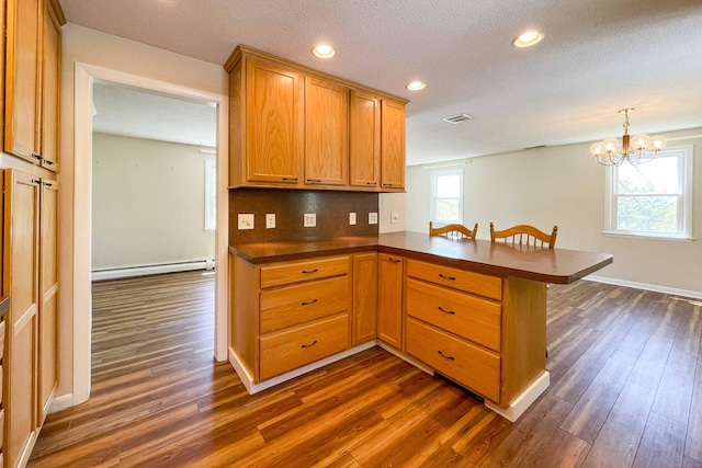 kitchen with visible vents, dark countertops, baseboard heating, a peninsula, and dark wood-style floors