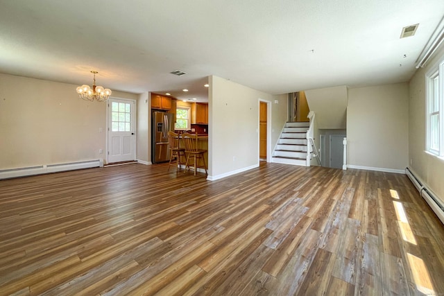 unfurnished living room featuring an inviting chandelier, stairs, wood finished floors, and visible vents