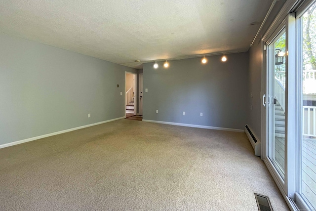 empty room with rail lighting, baseboard heating, stairs, and light carpet