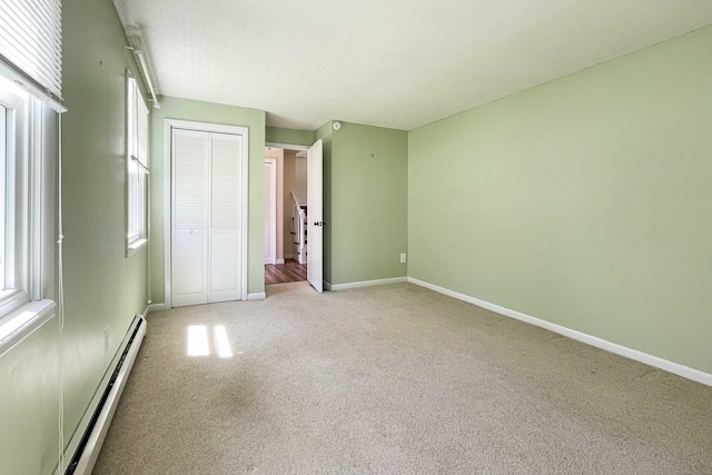 unfurnished bedroom with a closet, a baseboard radiator, baseboards, and carpet flooring