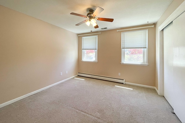 empty room featuring a ceiling fan, a baseboard heating unit, carpet flooring, and visible vents