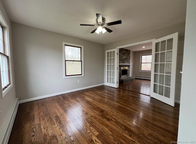 unfurnished living room with dark wood finished floors, a baseboard heating unit, a wealth of natural light, and a baseboard radiator