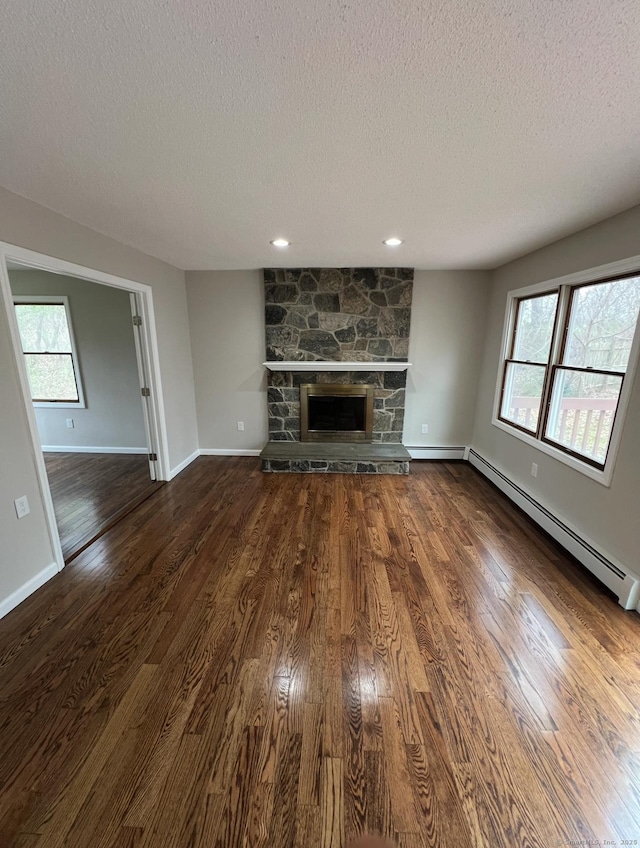 unfurnished living room featuring dark wood-style flooring, baseboard heating, a fireplace, a textured ceiling, and baseboards