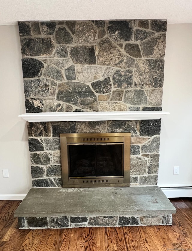 details featuring a stone fireplace, wood finished floors, and a baseboard radiator