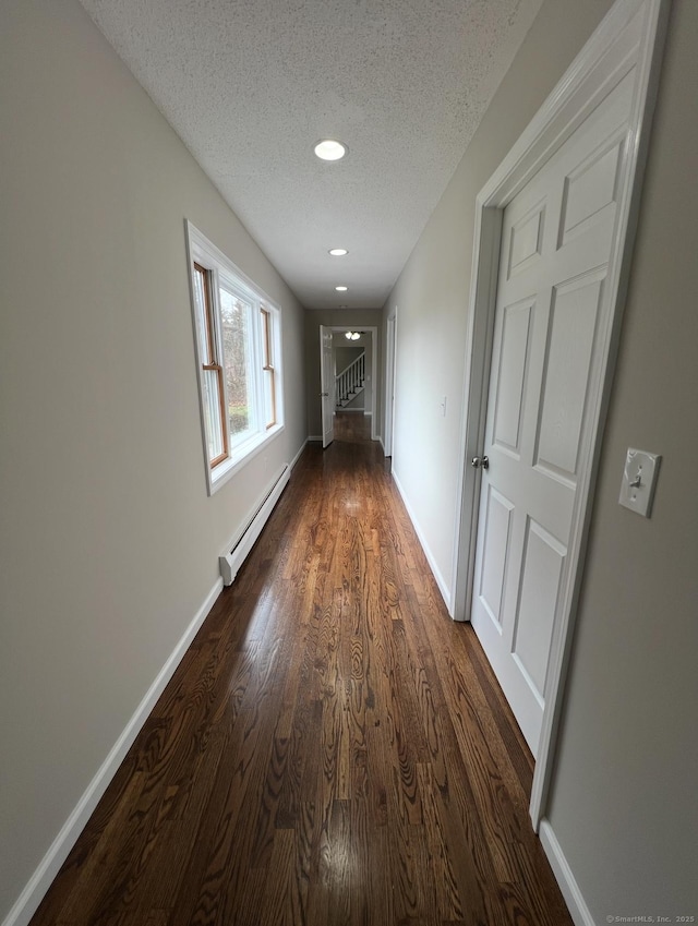 corridor with baseboards, a baseboard radiator, a textured ceiling, and dark wood finished floors