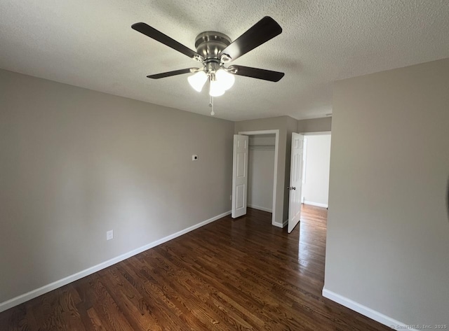 unfurnished bedroom featuring ceiling fan, a textured ceiling, baseboards, a closet, and dark wood-style floors