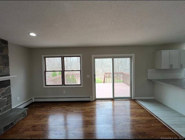 unfurnished living room with dark wood-style flooring, a stone fireplace, a textured ceiling, a baseboard heating unit, and recessed lighting
