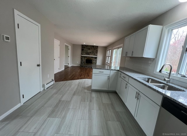 kitchen featuring a sink, stainless steel dishwasher, baseboard heating, and light stone countertops