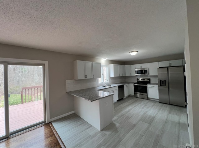 kitchen featuring a peninsula, a textured ceiling, appliances with stainless steel finishes, and a sink