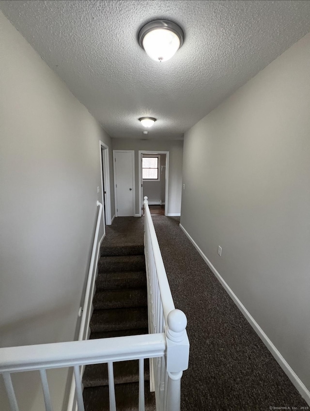 stairway featuring baseboards, carpet flooring, and a textured ceiling