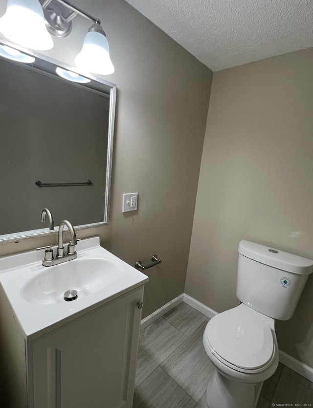 half bathroom featuring vanity, baseboards, toilet, and a textured ceiling