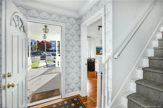 foyer with wallpapered walls, wood finished floors, stairway, and crown molding
