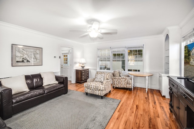 living room featuring ornamental molding, ceiling fan, light wood-style flooring, and a wainscoted wall