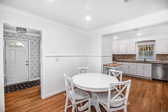 dining area with light wood-type flooring, a wainscoted wall, and ornamental molding