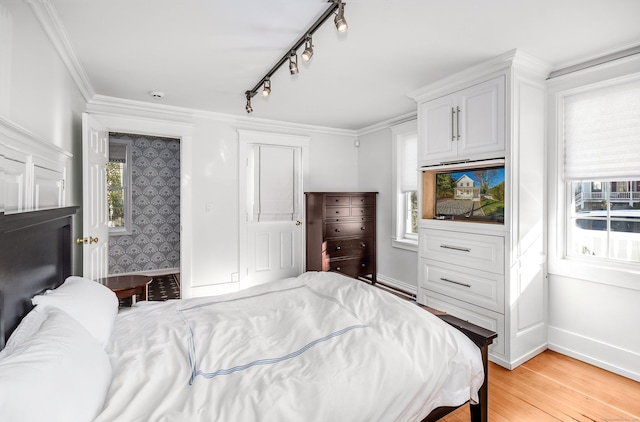 bedroom featuring light wood finished floors, multiple windows, baseboards, track lighting, and crown molding