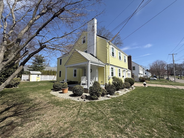 view of side of property featuring a lawn, a shed, covered porch, and a chimney