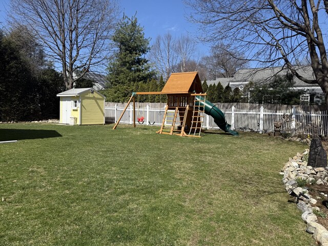 view of yard with a storage unit, a fenced backyard, a playground, and an outbuilding