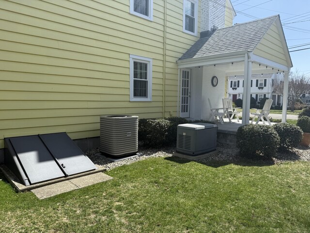 back of house with roof with shingles, central AC unit, and a yard