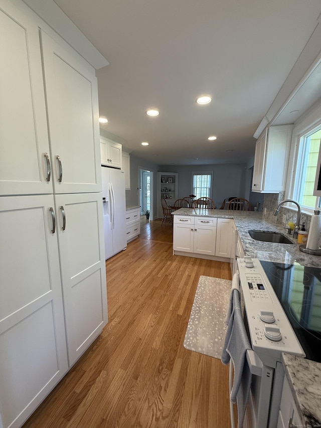 kitchen with light wood-type flooring, a sink, white cabinets, white fridge with ice dispenser, and recessed lighting