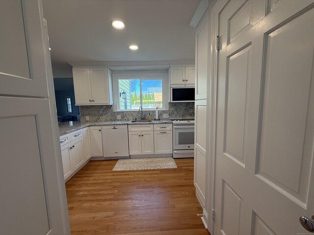 kitchen with a sink, white appliances, light wood-style flooring, white cabinetry, and recessed lighting