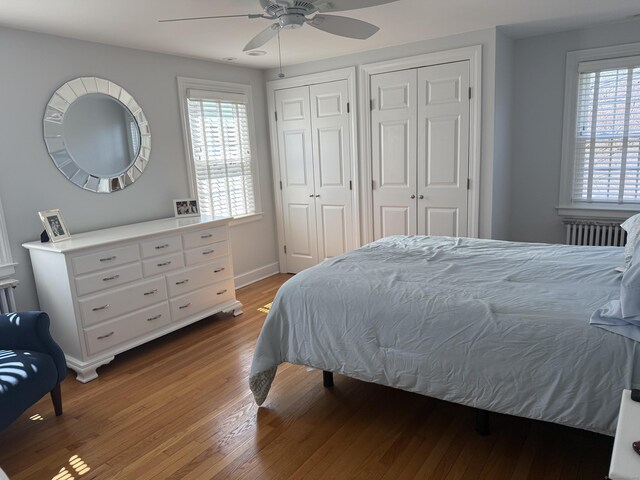 bedroom with radiator, multiple closets, wood finished floors, baseboards, and ceiling fan