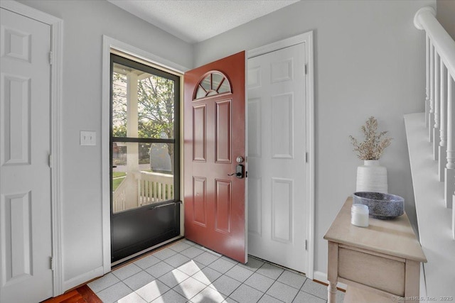 foyer with light tile patterned floors, baseboards, stairs, and a textured ceiling