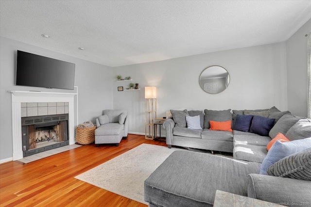 living area with a textured ceiling, a tiled fireplace, and wood finished floors