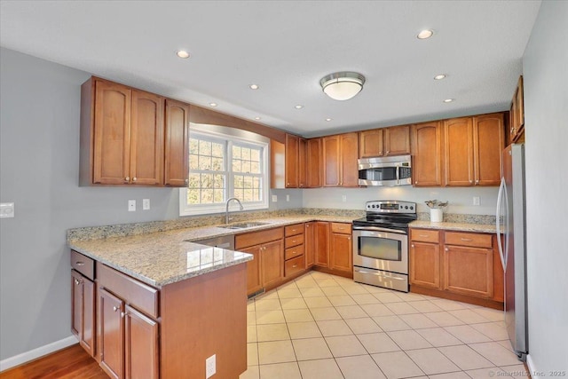 kitchen with appliances with stainless steel finishes, light stone countertops, brown cabinets, a sink, and a peninsula
