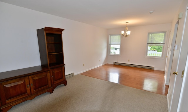 carpeted empty room featuring a baseboard heating unit, a chandelier, and wood finished floors