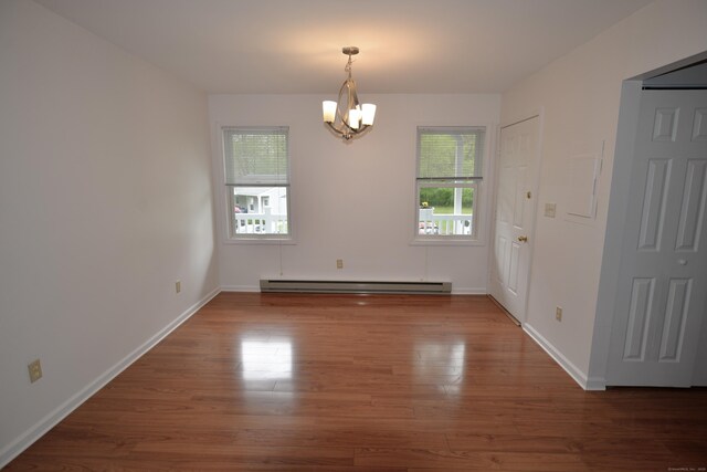 unfurnished dining area with a baseboard heating unit, a chandelier, wood finished floors, and baseboards