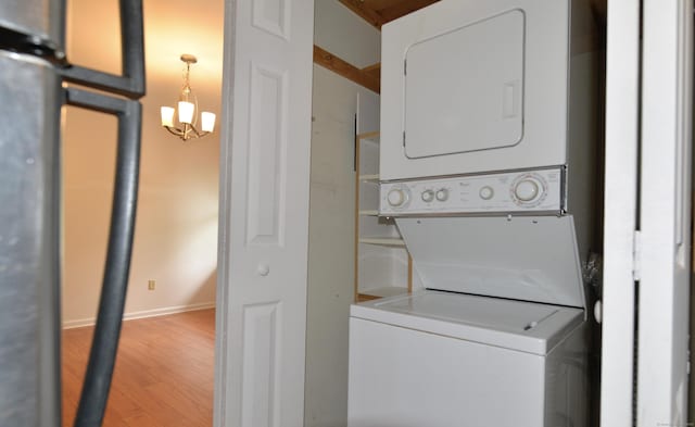 washroom featuring stacked washing machine and dryer, light wood-type flooring, baseboards, and a chandelier