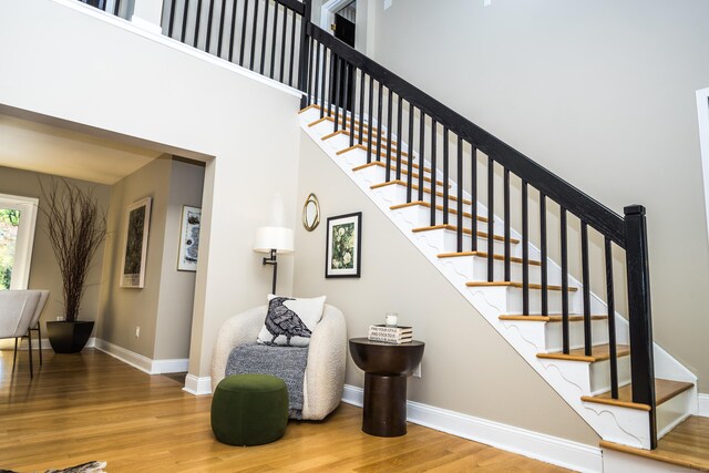 staircase featuring baseboards, a high ceiling, and wood finished floors