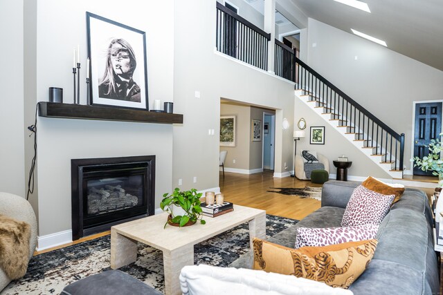 living area with a high ceiling, a glass covered fireplace, baseboards, wood finished floors, and stairway