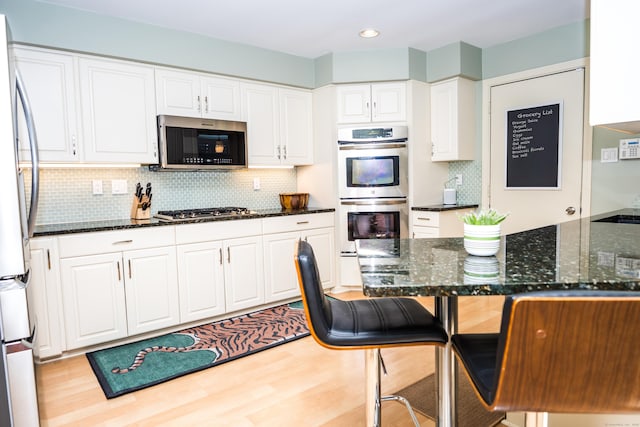 kitchen featuring backsplash, a kitchen bar, dark stone countertops, stainless steel appliances, and white cabinetry