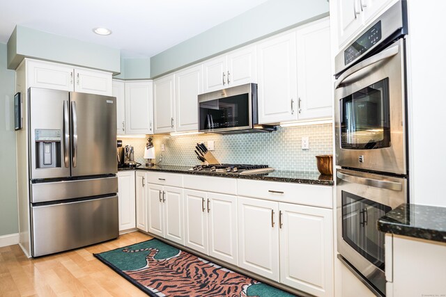 kitchen with light wood-style floors, dark stone counters, white cabinetry, appliances with stainless steel finishes, and backsplash