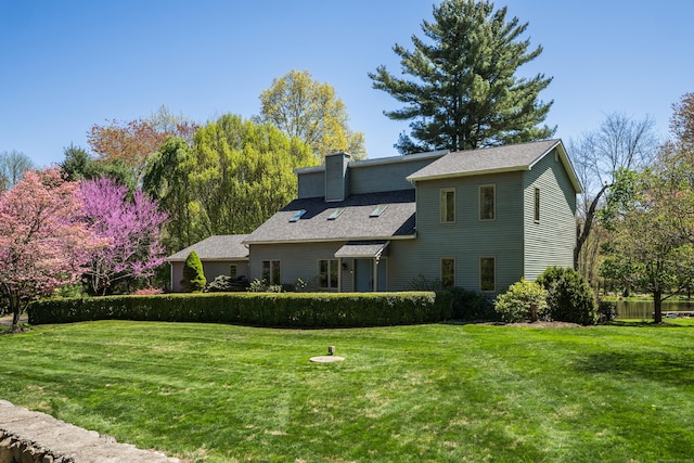rear view of property featuring roof with shingles, a yard, and a chimney