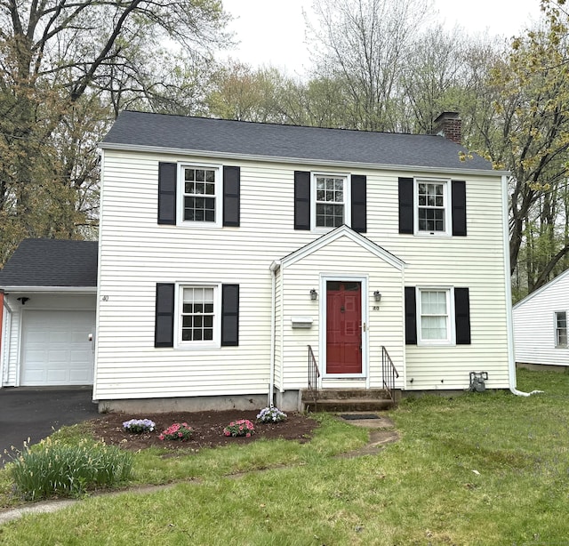 colonial house featuring an attached garage, aphalt driveway, a front yard, entry steps, and a chimney